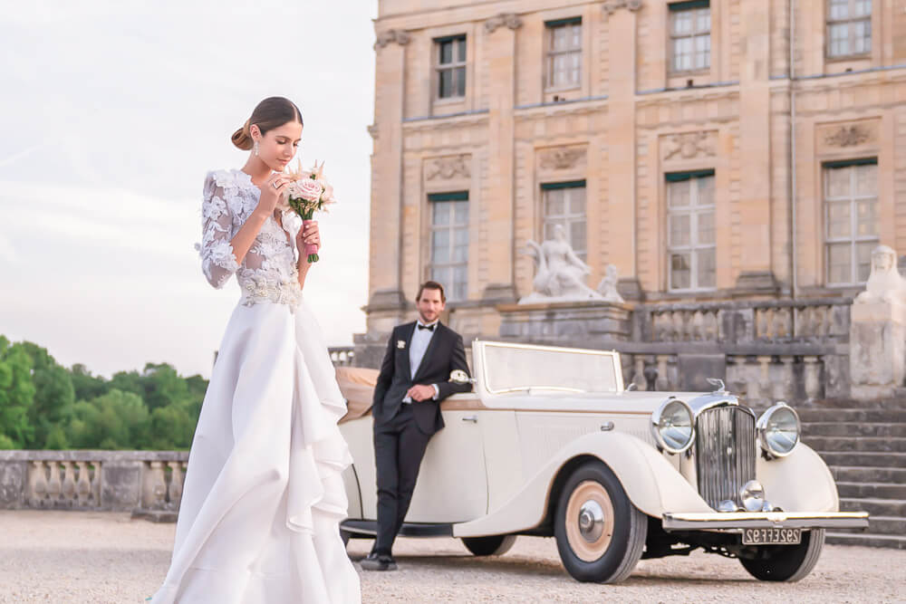 Stylish couple posing with vintage car at Chateau Vaux le Vicomte near Paris, France, as part of their Paris wedding