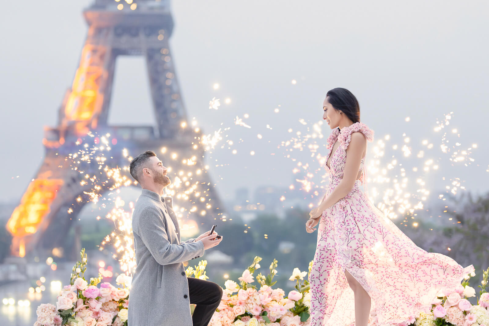 Enlisting a seasoned local Paris proposal planner is key to navigating the complexities of public hotspots like Trocadéro, as seen in this legendary Eiffel Tower proposal. Here, a stylish couple steals the show as the gentleman drops to one knee, presenting a ring box to his sweetheart, surrounded by stunning florals and sparkling fireworks—a truly magical ambiance.