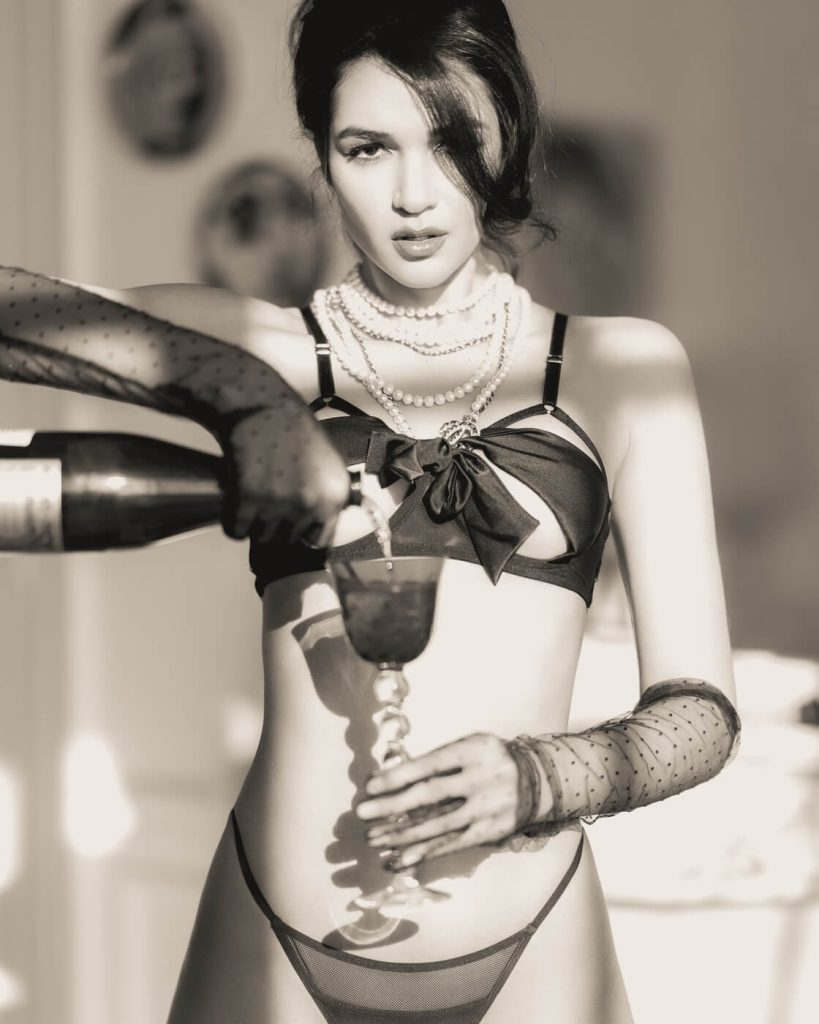 Indulge in Parisian glamour with a boudoir photoshoot that exudes sophistication and allure. This captivating black and white image captures a woman in luxurious lingerie, playfully pouring a glass of champagne (crystal glass by Saint Louis, bien sûr 😉 ) with a suggestive gaze. The elegant setting of a Parisian loft adds to the atmosphere of refined sensuality.