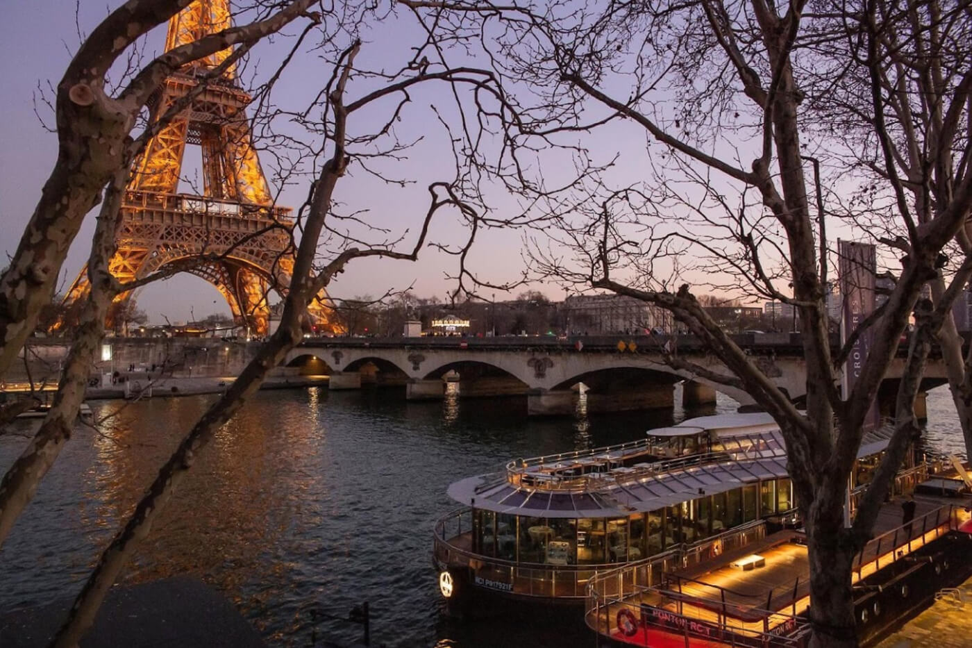 Ducasse sur Seine's illuminated boat docked at night with the glittering Eiffel Tower as backdrop