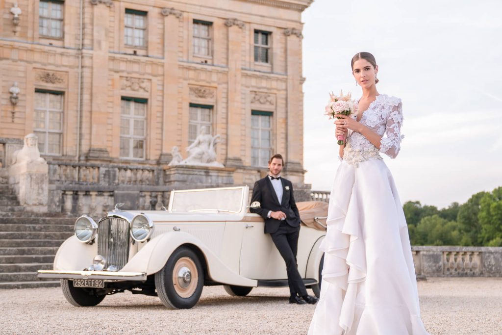 Luxury Paris wedding photography at Chateau Vaux-le-Vicomte: elegant bride with royal bouquet, groom leaning on vintage convertible, castle backdrop