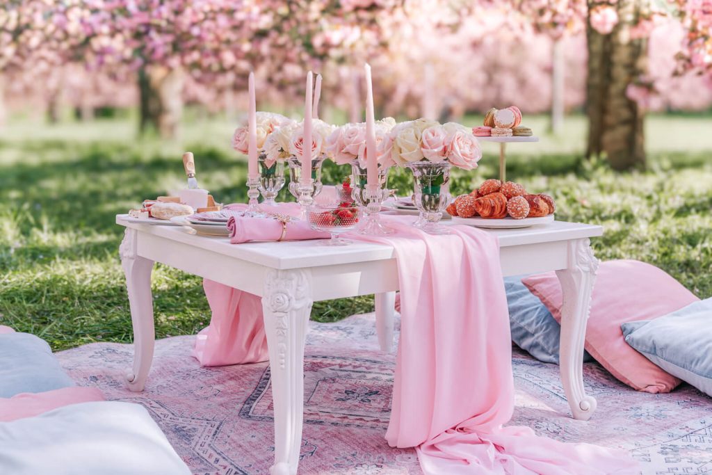 Luxury Paris picnic photography: vintage white table with fine linens, pastries, and flowers under blooming cherry blossoms at Parc de Sceaux, perfect for romantic portraits and family photos