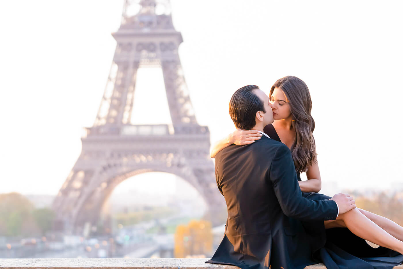 Romantic Paris portrait session at Trocadero: stylish couple kissing on wall with golden sunrise illuminating Eiffel Tower backdrop, perfect for couple photography