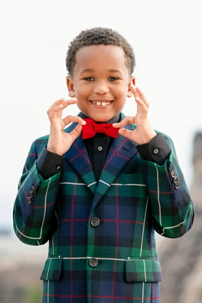 Young boy at Trocadero adjusting his red bow tie and looking at the camera during a Paris family photography session
