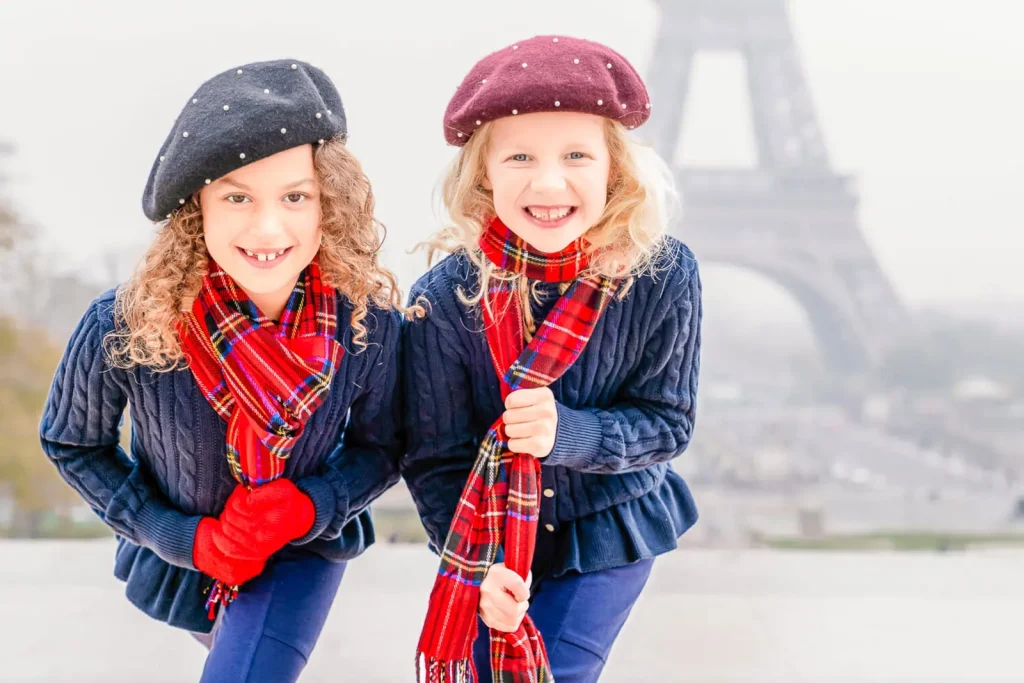 Paris family photographer captures two stylish girls looking at camera at Trocadero with blurred Eiffel Tower background - professional family portrait photography