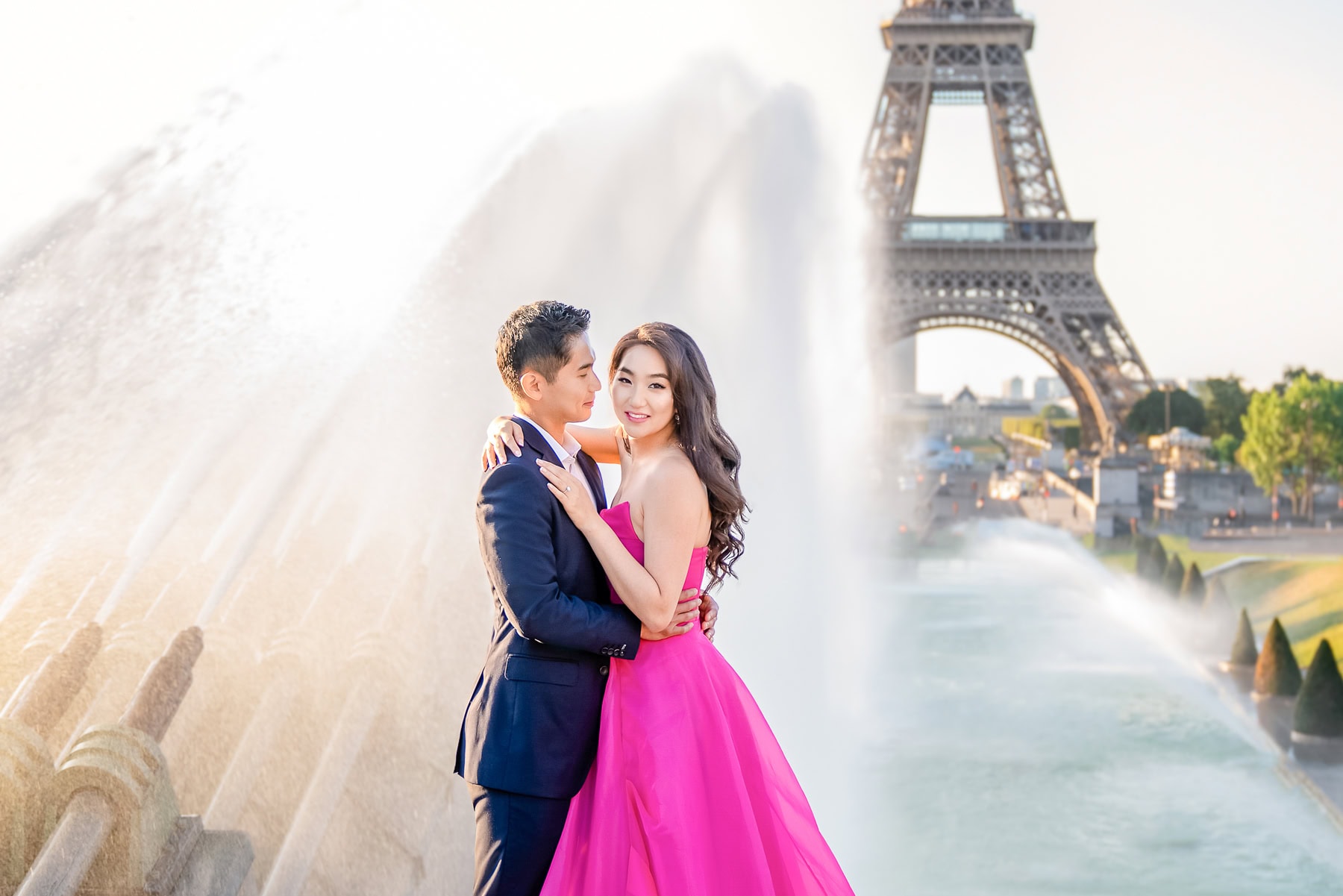 A stylish couple poses at the Trocadéro fountains during a sunrise photoshoot with the Eiffel Tower in the background.