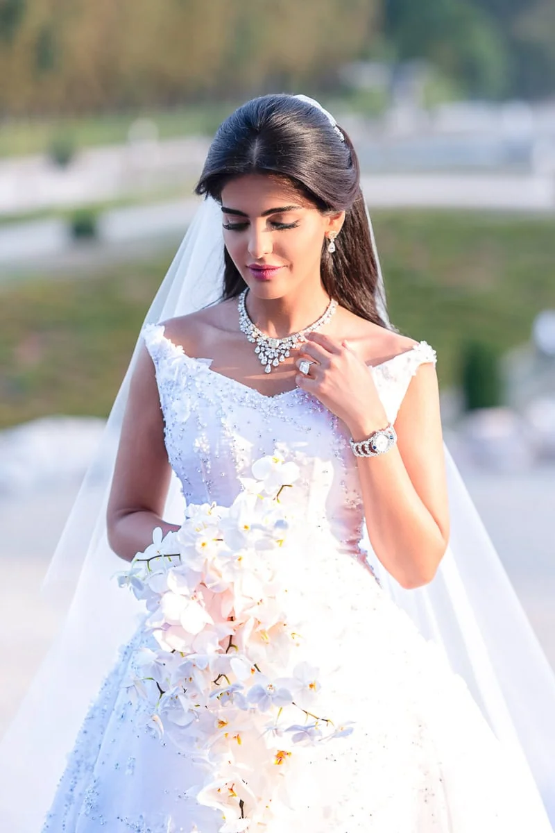 Bride in Dior Couture adjusts her diamond necklace at Chateau Vaux le Vicomte, captured by our Paris wedding photographer.