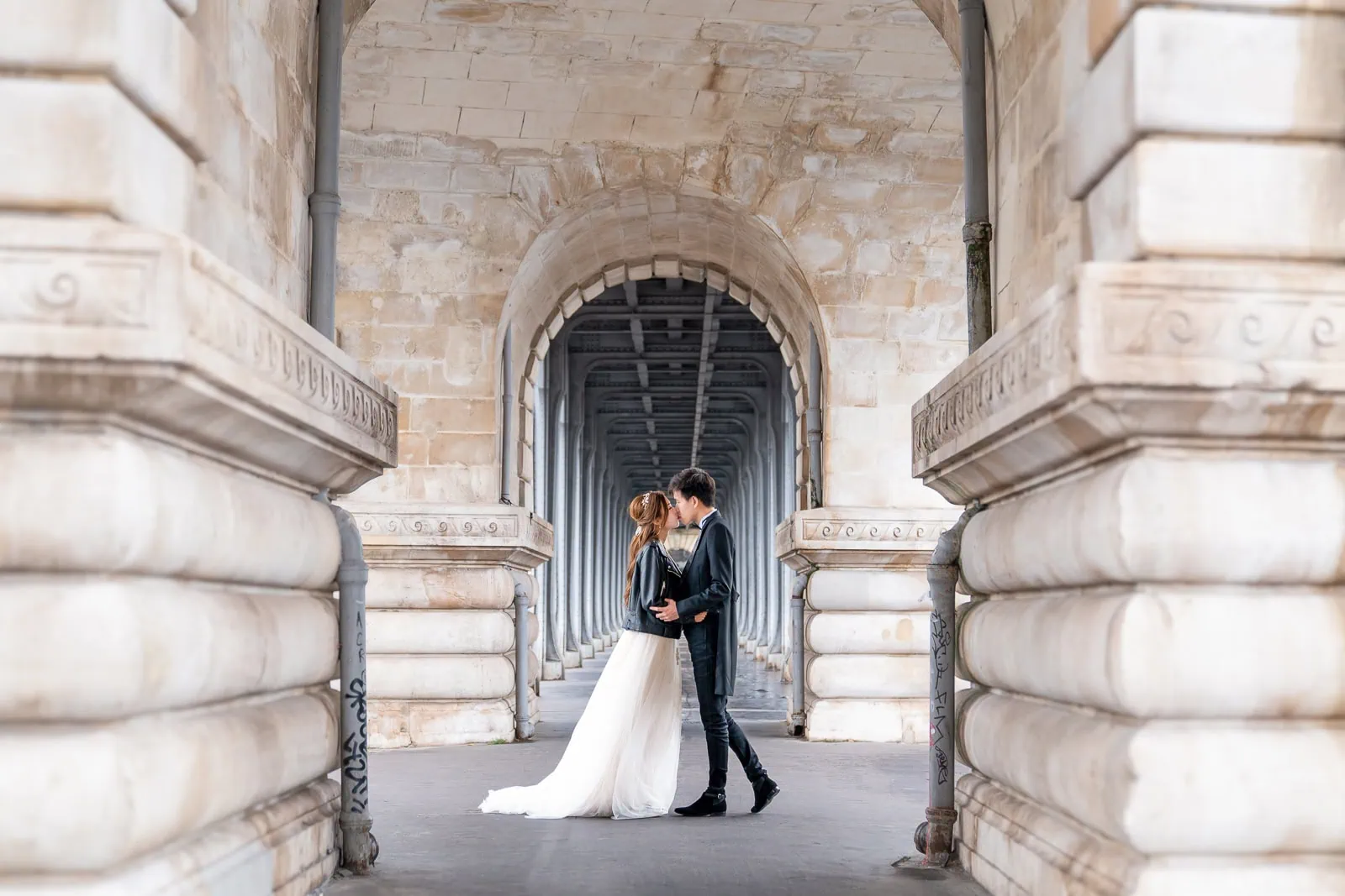 Pre-wedding couple kissing under Bir Hakeim Bridge infinity arches at sunrise in Paris