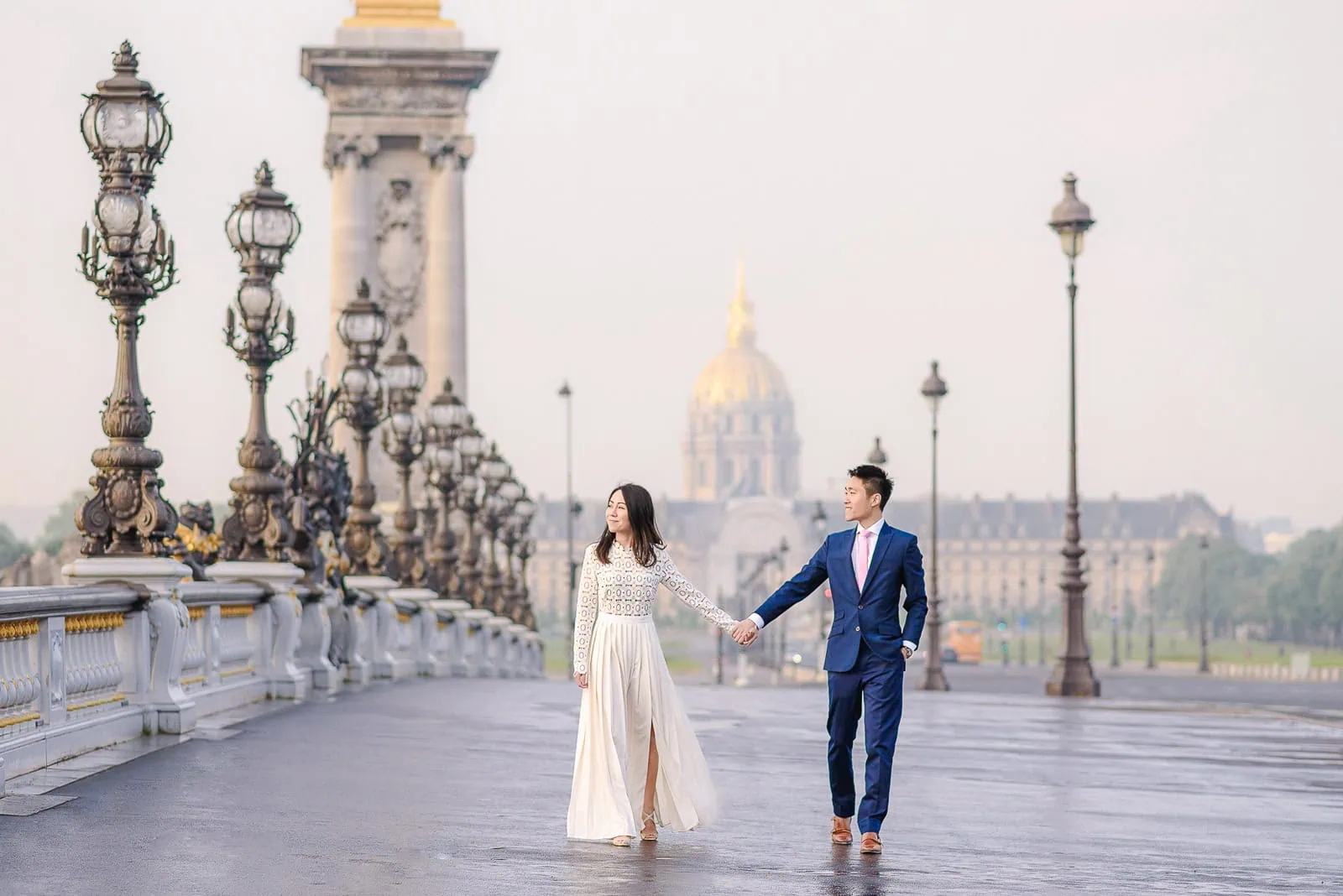 Couple walking toward camera at Alexander III Bridge sunrise with Les Invalides backdrop Paris