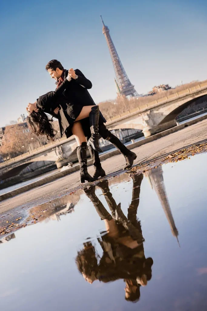 Couple editorial dip pose at Pont Alexandre III after rain with puddle reflection showing Eiffel Tower, Paris engagement photographer